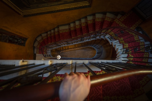 A photo looking down a staircase that curves around in an oval, with a hand on the bannister.